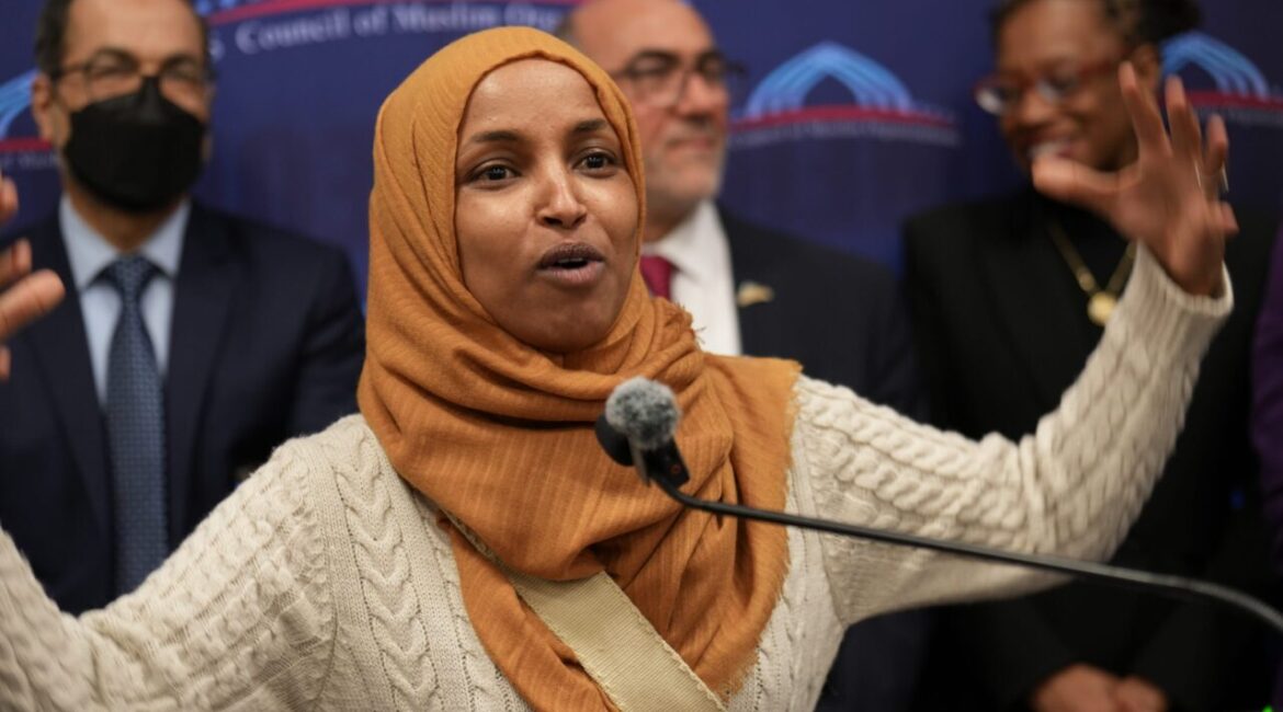 Image of Rep. Ilhan Omar speaking at the Capitol in Washington, D.C. She's wearing a oak-colored knit sweater with a caramel colored hijab