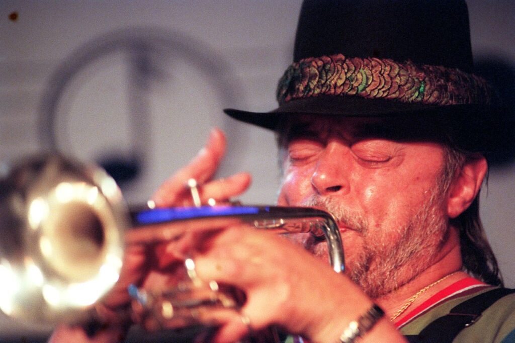 Image of Chuck Mangione blowing his trumpet. He's wearing a black hat with a multicolored band