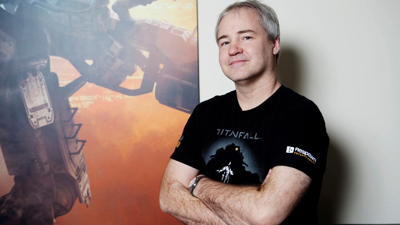 Image of video games designer Vince Zampella. He's wearing a black t-shirt and has his arms folded while standing in front of a video game poster.