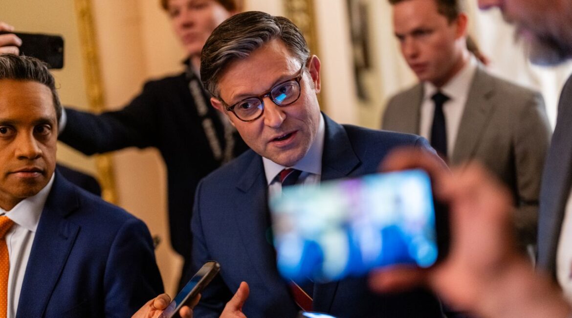 Image of House Speaker Mike Johnson in a blue suit talking to reporters about a health care bill. One reporter is videoing the Speaker with a cell phone