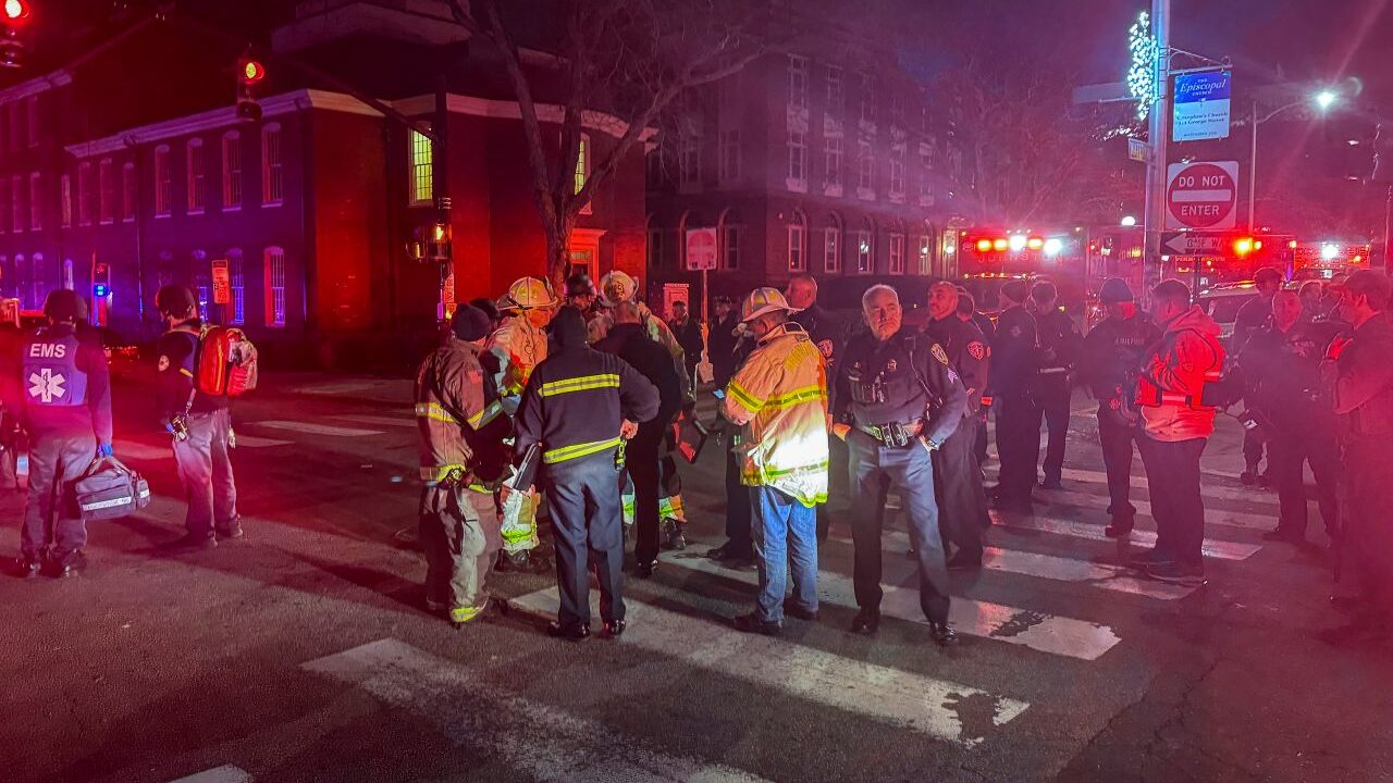 Image of first responders at the scene of a shooting at Brown University at night. The emergency responder vehicle lights cast a red pall over the scene.