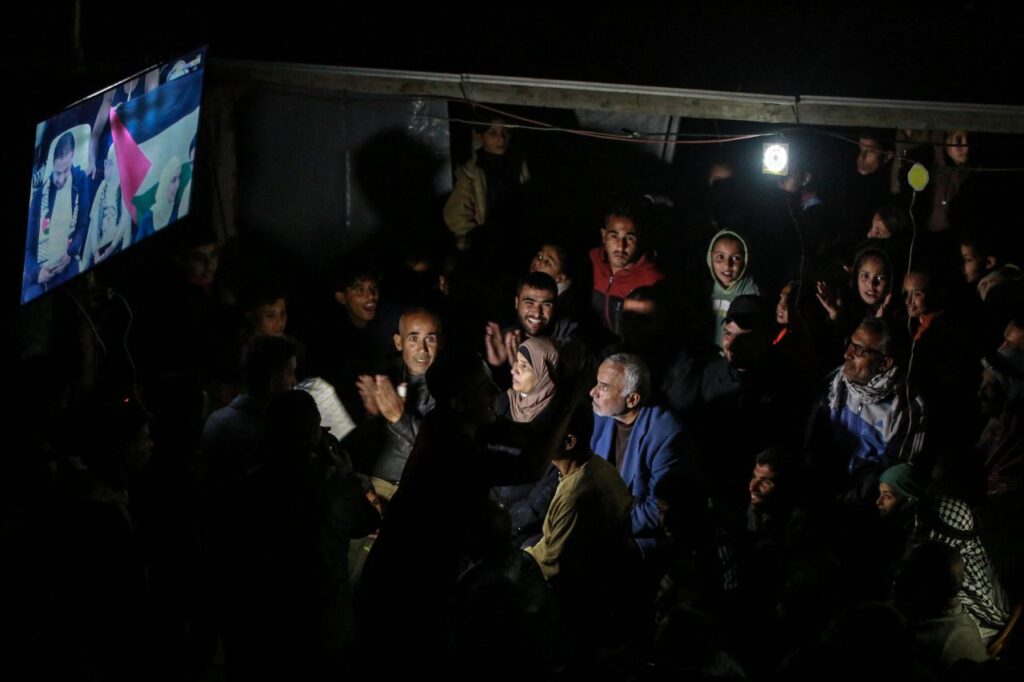 Image of Palestinians crowding around a TV screen to watch their national soccer team play Saudi Arabia. 