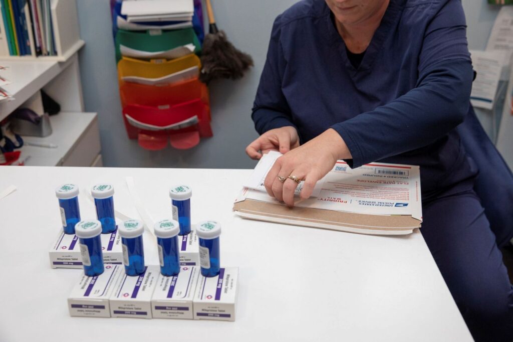 A woman in dark-color scrubs inventories pharmacy containers of mifepristone and misoprostol pills that will be mailed to patients seeking at-home abortions.