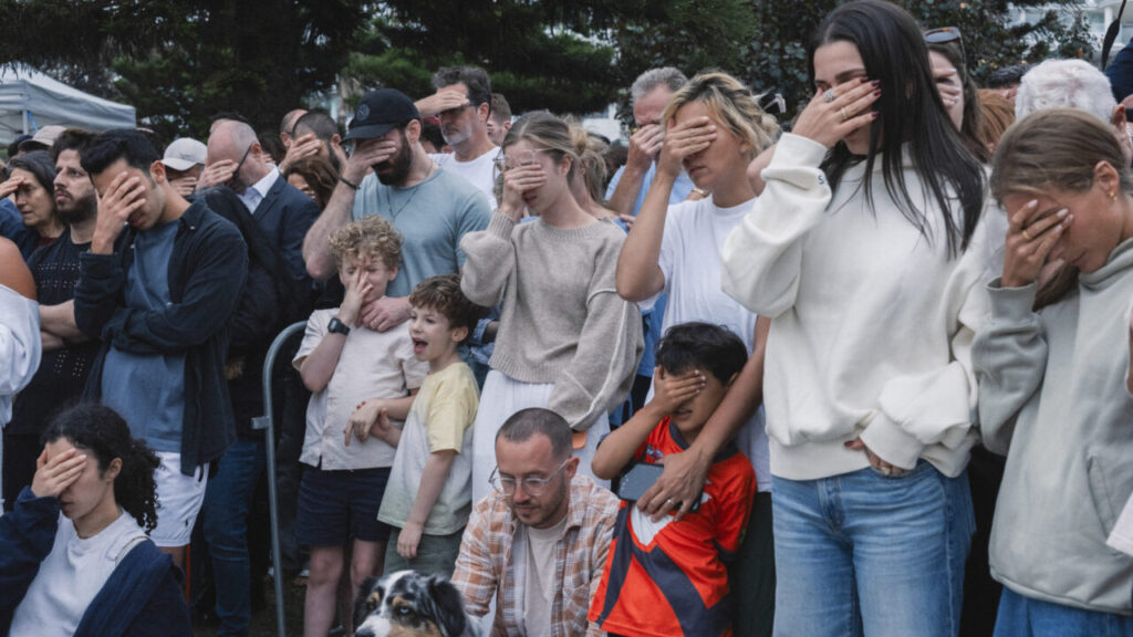 Image of mourners covering their eyes while praying for those killed in a mass shooting in Australia