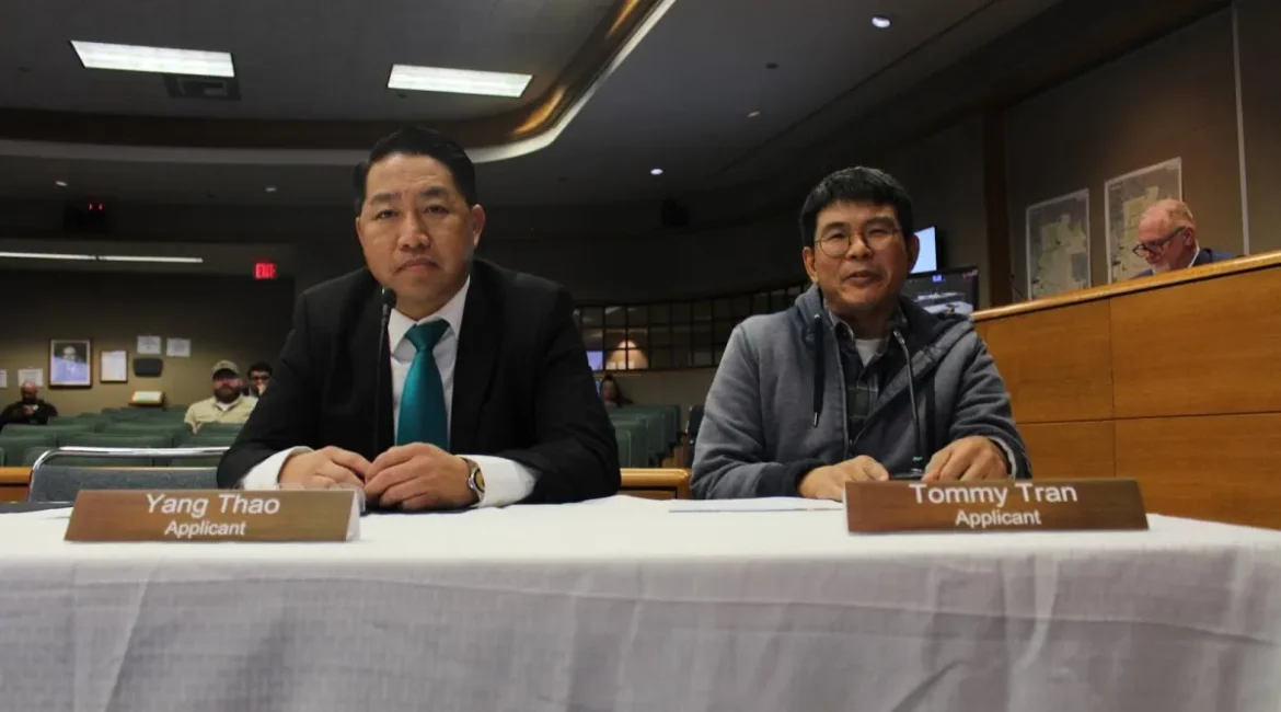 Images if Yang Thao and Tommy Tran sitting at a table covered with a white sheet inside Merced City Council chambers