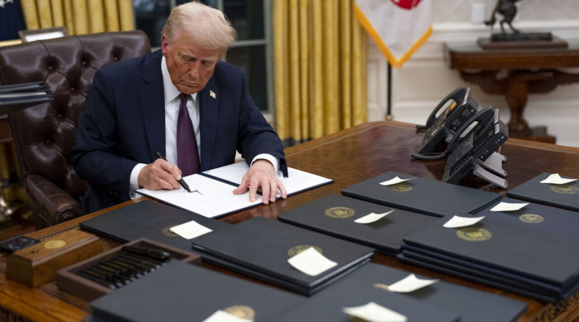 Image of President Trump at his Oval Office desk signing presidential pardons on the first day of his second term