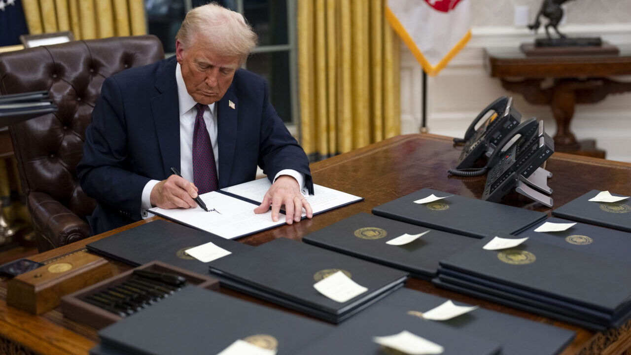Image of President Trump at his Oval Office desk signing presidential pardons on the first day of his second term