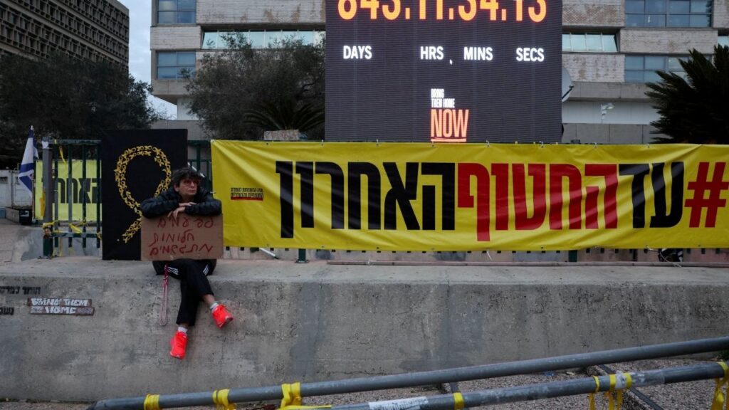 A person holding a placard reading "Sometimes dreams come true" sits next to a banner reading "Until the last hostage", on the day the iconic clock timer is to be turned off, after marking 844 days of hostage captivity and the return of the Israel's last remaining hostage in Gaza, Ran Gvili, an off-duty police officer who was killed fighting militants that had infiltrated Israel during the deadly October 7, 2023 attack by Hamas, in "Hostages Square" in Tel Aviv, Israel, January 27, 2026. (Reuters/Nir Elias)
