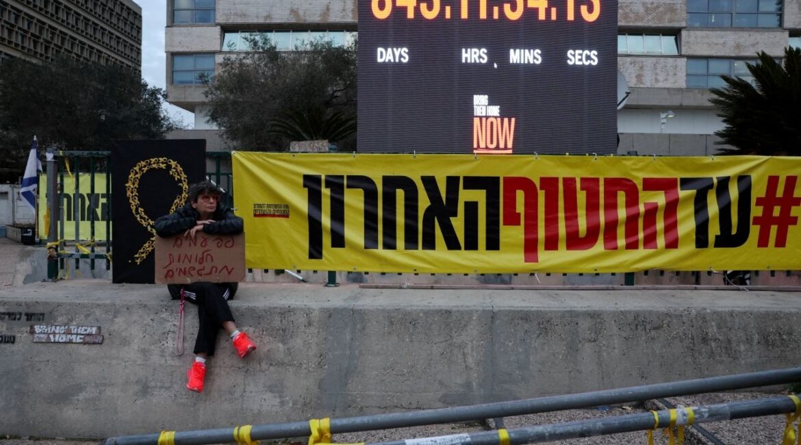 A person holding a placard reading "Sometimes dreams come true" sits next to a banner reading "Until the last hostage", on the day the iconic clock timer is to be turned off, after marking 844 days of hostage captivity and the return of the Israel's last remaining hostage in Gaza, Ran Gvili, an off-duty police officer who was killed fighting militants that had infiltrated Israel during the deadly October 7, 2023 attack by Hamas, in "Hostages Square" in Tel Aviv, Israel, January 27, 2026. (Reuters/Nir Elias)