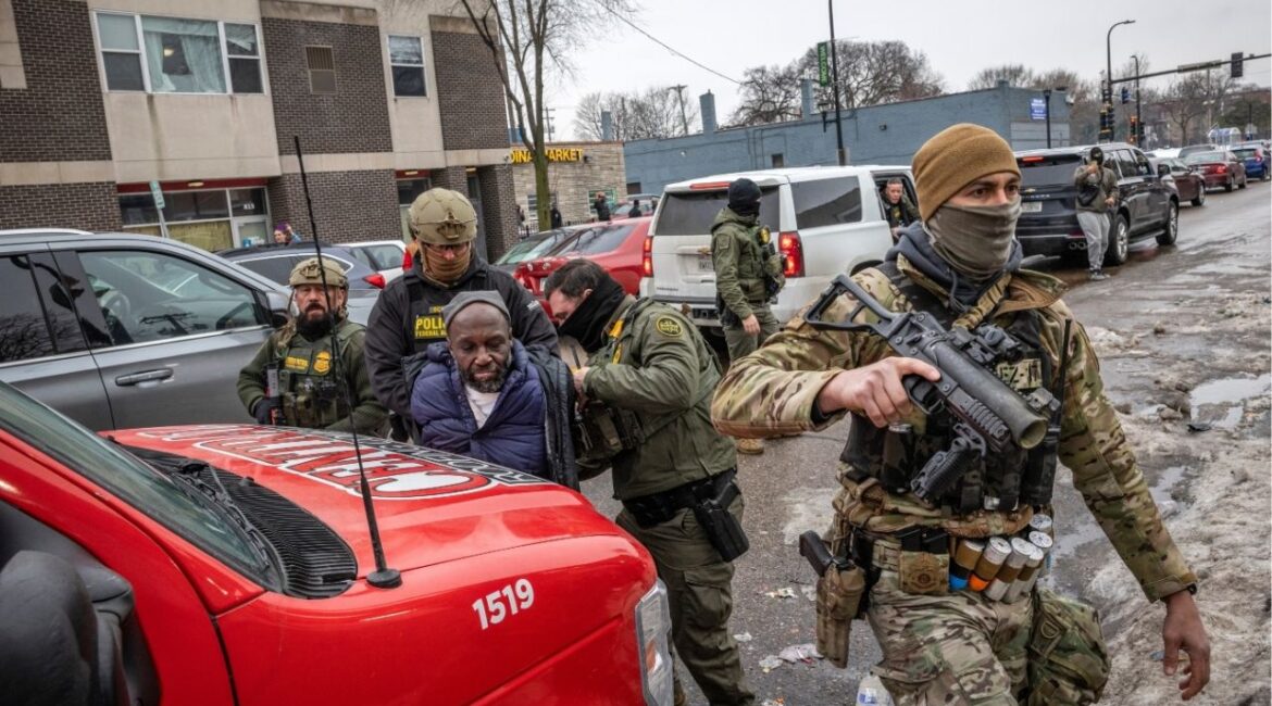 Federal agents arrest a man as Gregory Bovino, a senior Border Patrol official, exits a vehicle at rear in downtown Minneapolis, on Thursday, Jan. 8, 2026. Federal officers fired tear gas and pushed early-morning protesters back from their staging area, as outrage mounted in the city over the killing of a 37-year-old woman in her car. (David Guttenfelder/The New York Times)