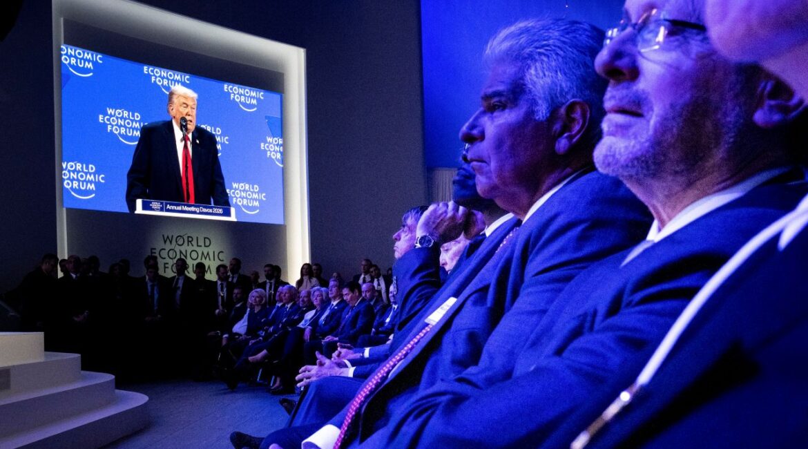 Image of members of the World Economic Forum viewing a speech by Donald Trump on a screen. The room is cast in a blue hue.