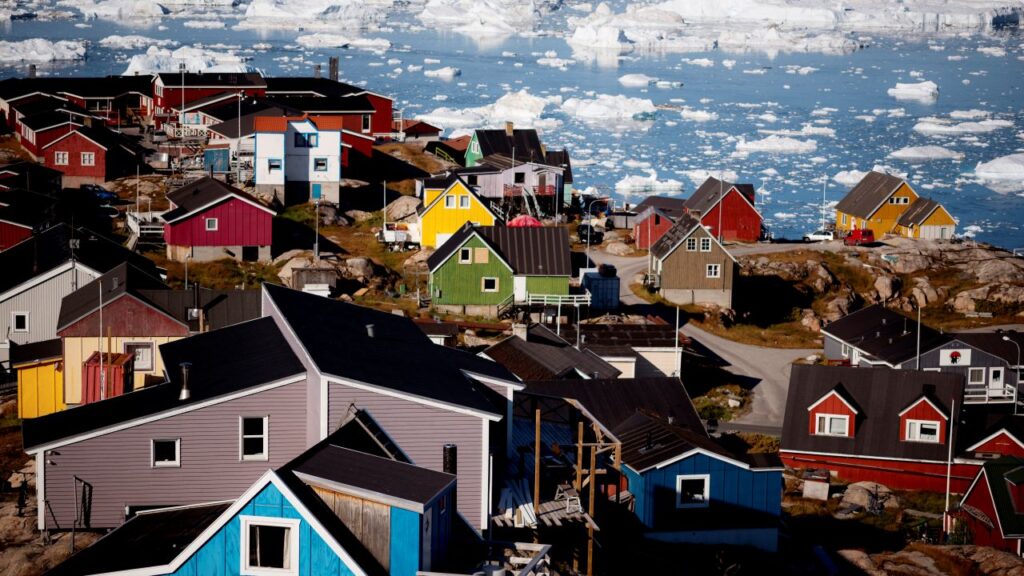 Image of the town of Ilulisat in Greenland against a backdrop of icebergs. The homes are painted in bright colors.
