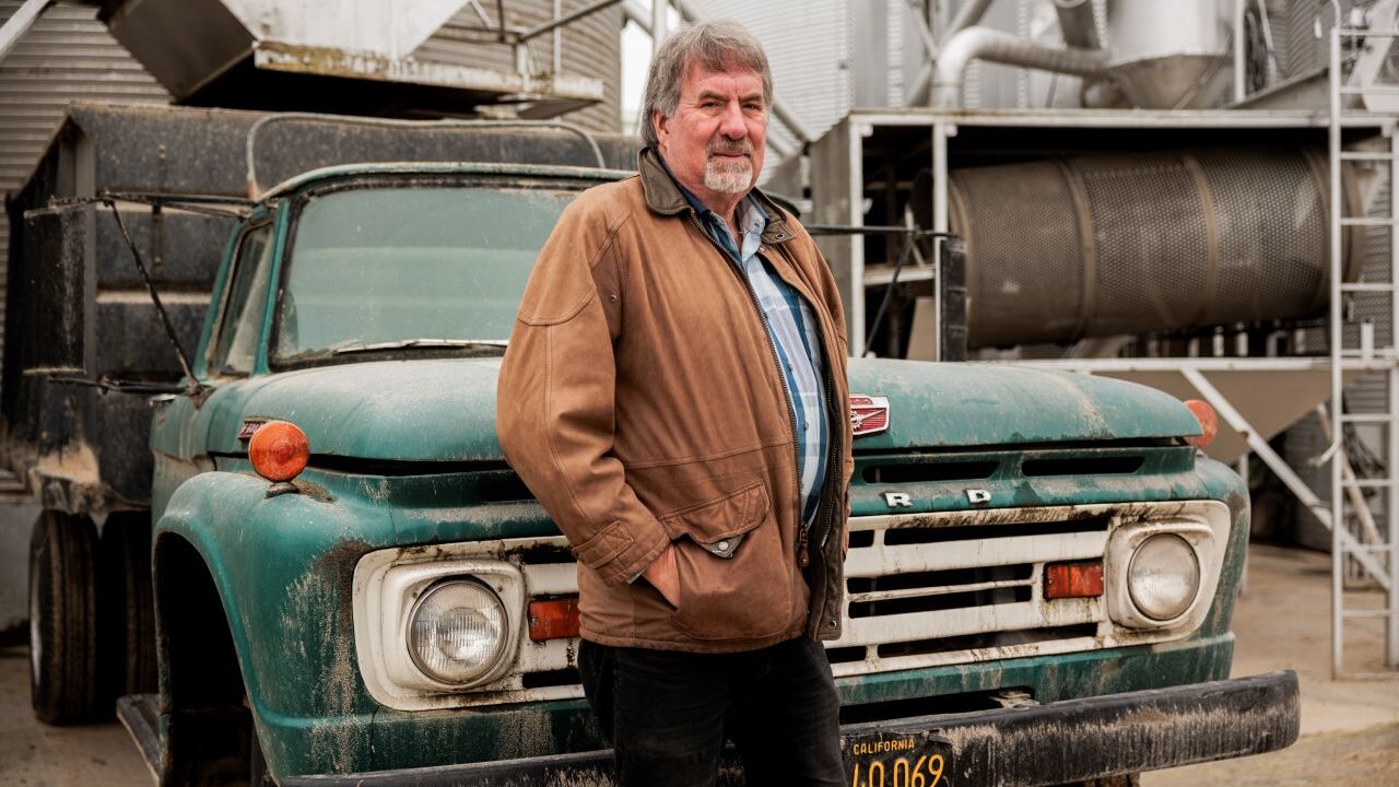 Image of the late Rep. Doug LaMalfa, a Republican, at his rice farm in Richvale. He's wearing a barn jacket and standing in front of a green Ford flatbed truck.