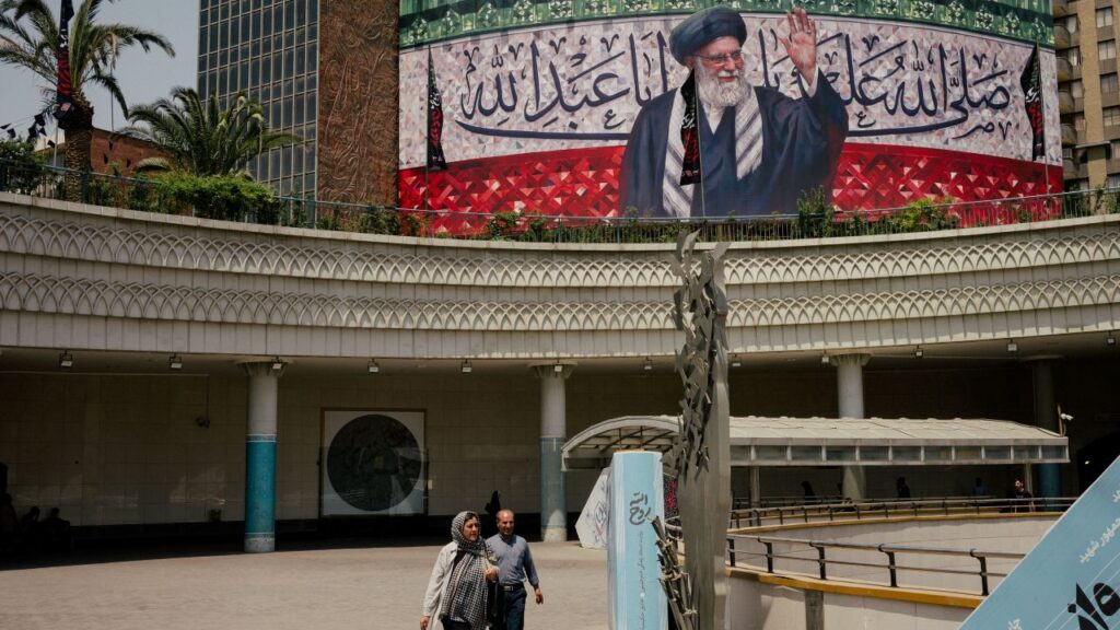 A billboard featuring a likeness of Iran’s Supreme Leader, Ayatollah Ali Khamenei, in s Tehran public area. Khamenei is in robes and raising his hand.