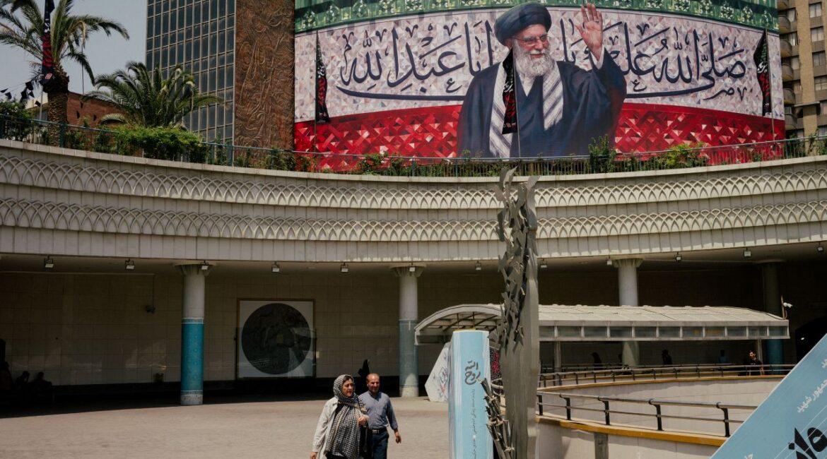 A billboard featuring a likeness of Iran’s Supreme Leader, Ayatollah Ali Khamenei, in s Tehran public area. Khamenei is in robes and raising his hand.
