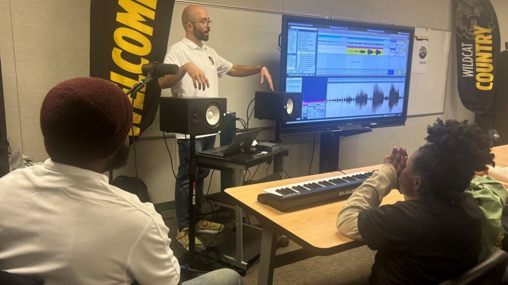 Image of a music teacher standing at the front of the classroom teaching his students.