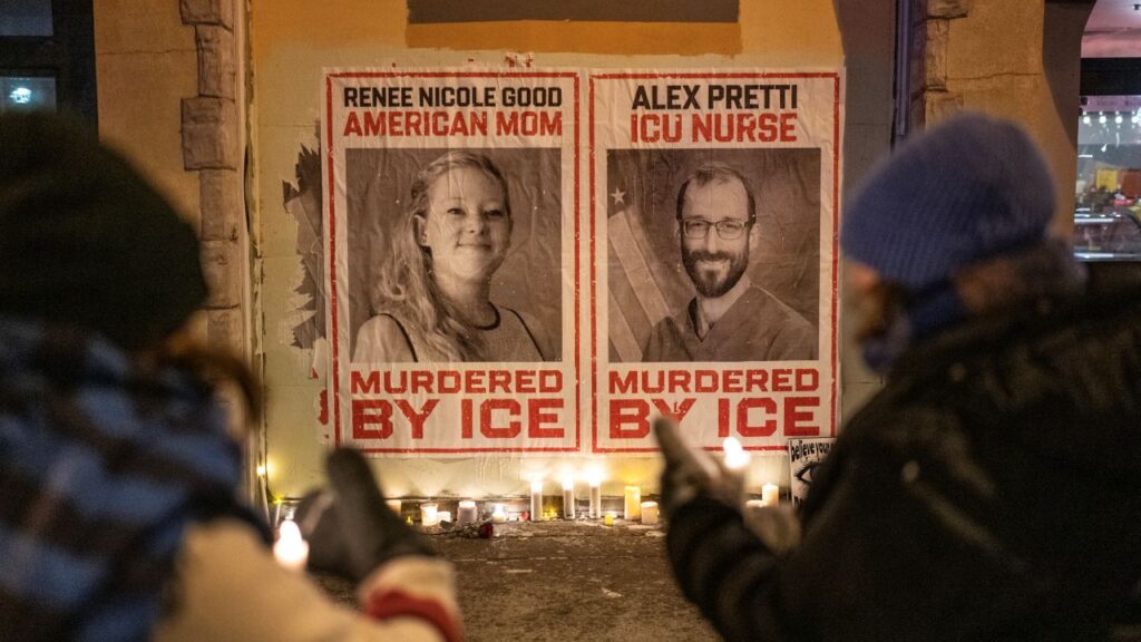 Image of mourners placing candles under posters of Renee Good and Alex Pretti on a cold night in Minneapolis.