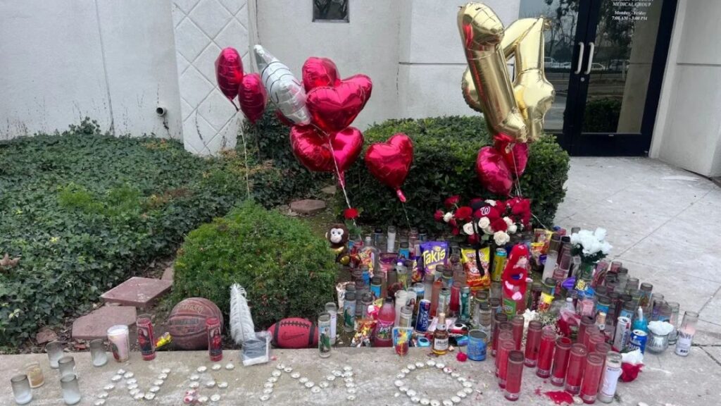 Image of a makeshift memorial with flowers, balloons, and chalk messages on a sidewalk