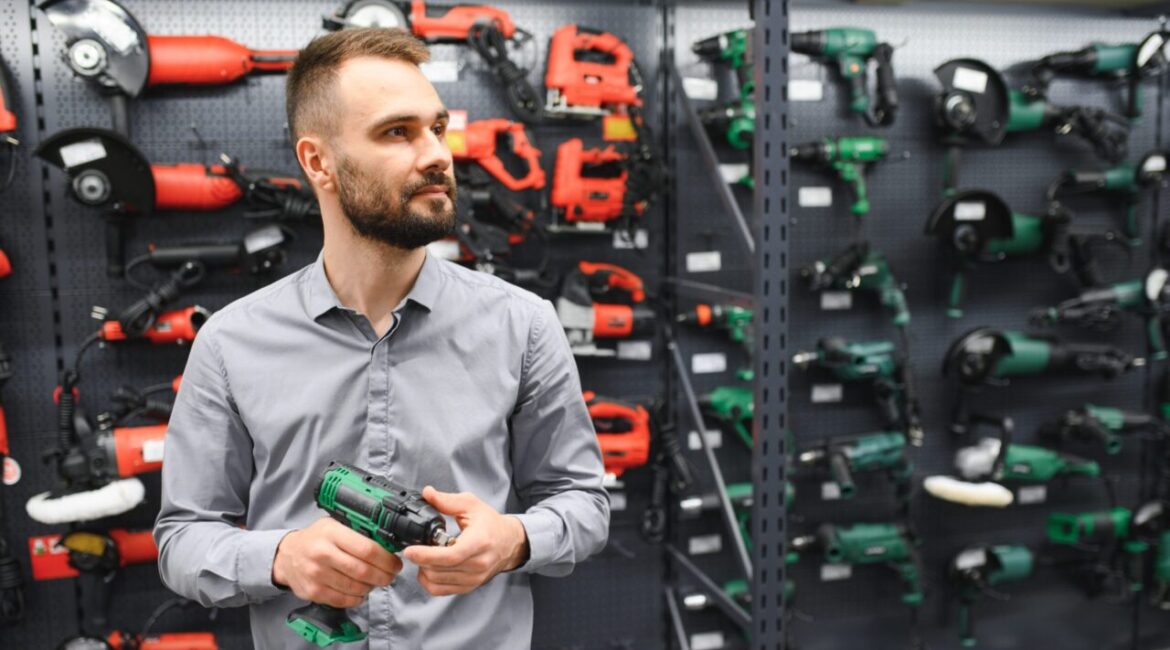 Image of a man in a gray shirt checking out which lithium battery powered drill to buy at a hardware store.