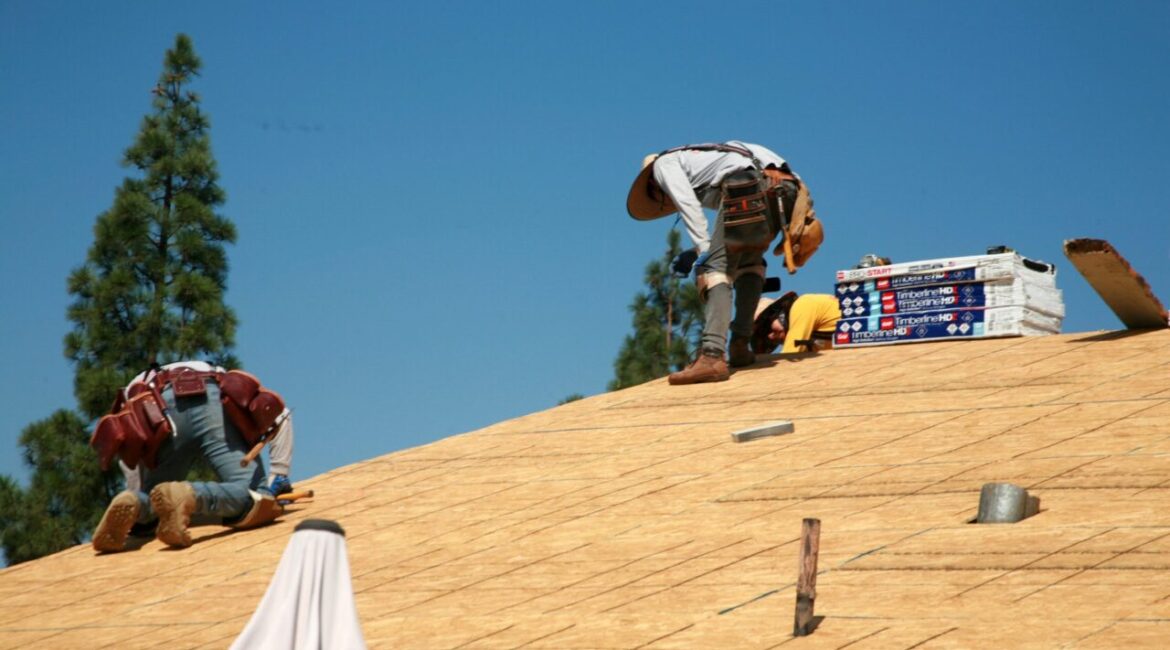 Image of workers atop a roof putting down plywood