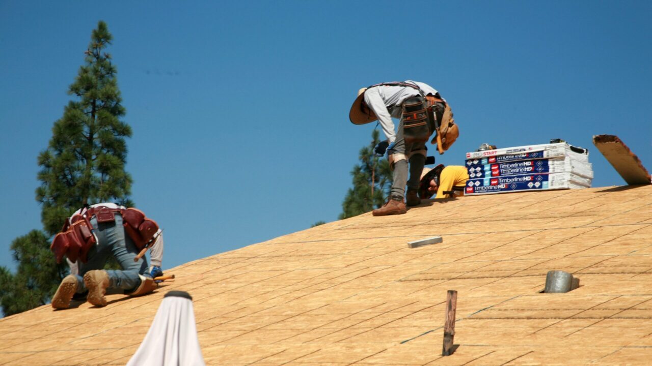 Image of workers atop a roof putting down plywood