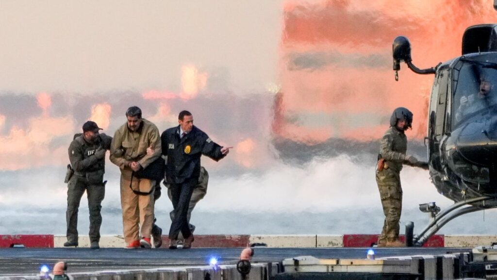 Image of a handcuffed Nicholas Madura and his wife being escorted away from a U.S. military helicopter in New York