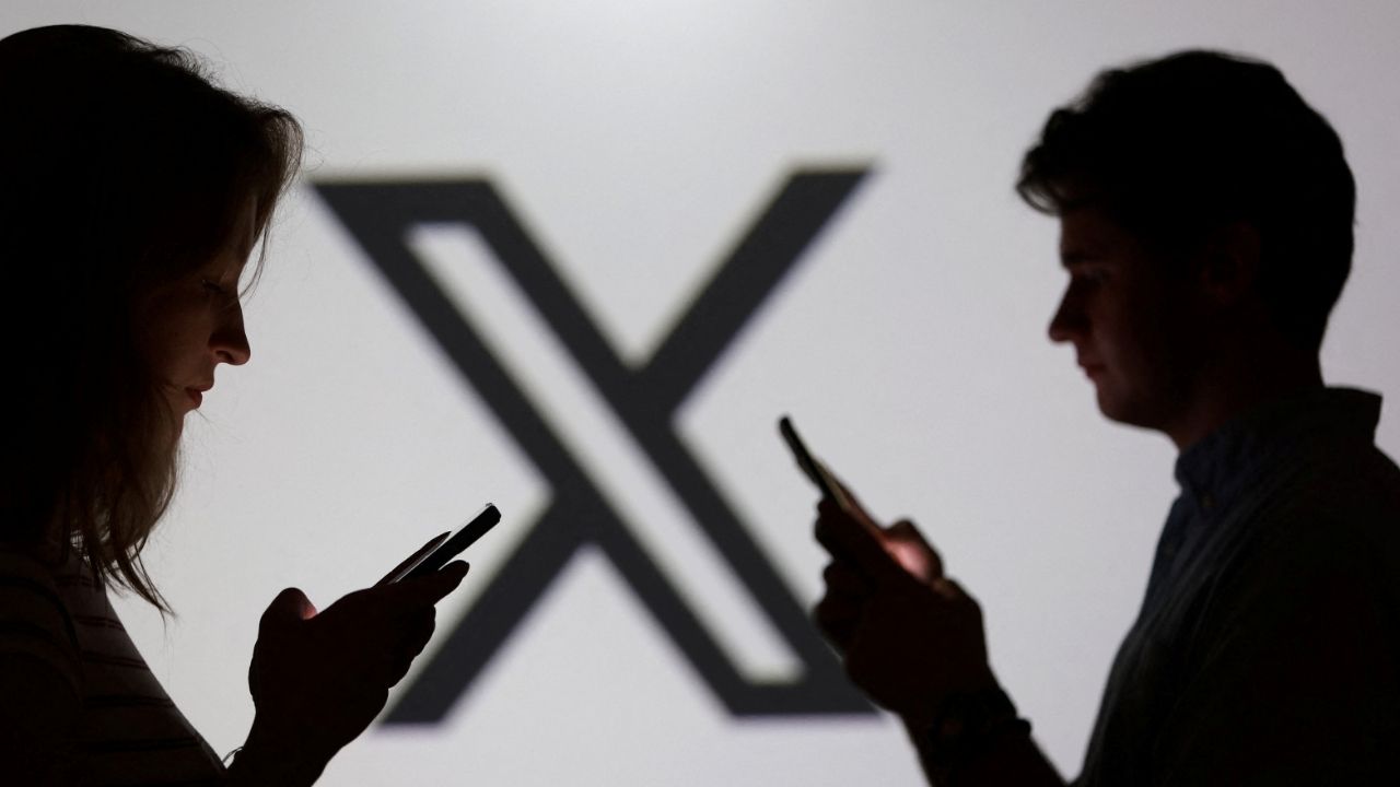Teenagers pose for a photo while holding smartphones in front of a X logo in this illustration taken September 11, 2025. (Reuters/Dado Ruvic/Illustration)
