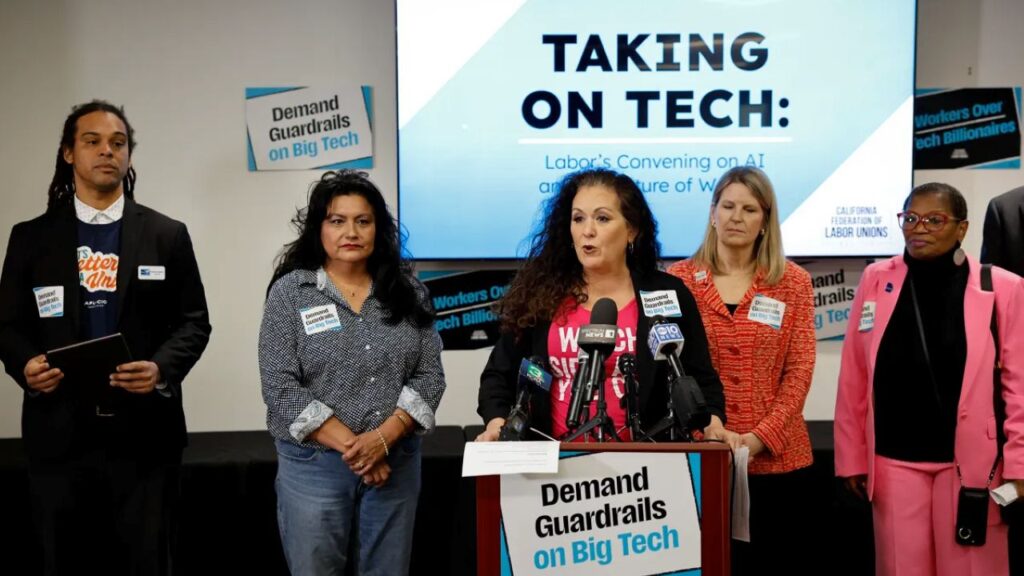Image of labor leader Lorena Gonzales, in blue jacket and red t-shirt, flanked by other union leaders