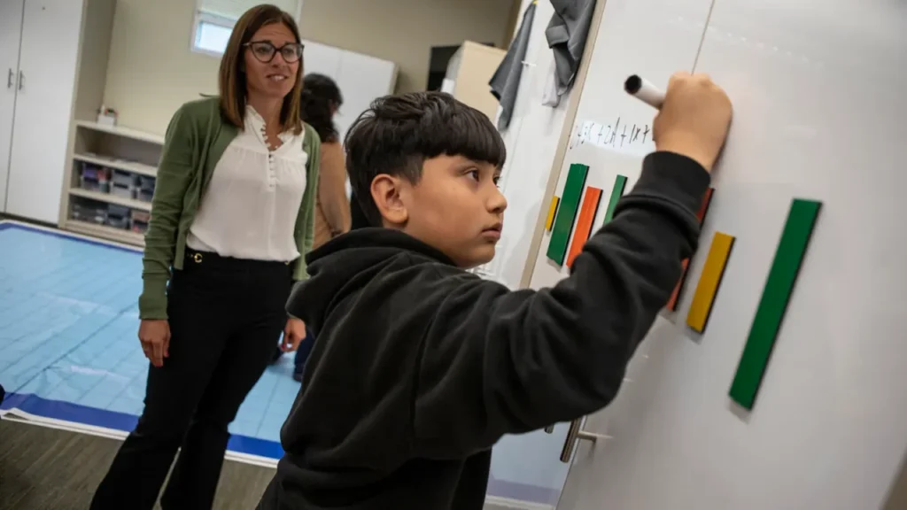 Image of a math coach helping a young male student who is writing on a whiteboard