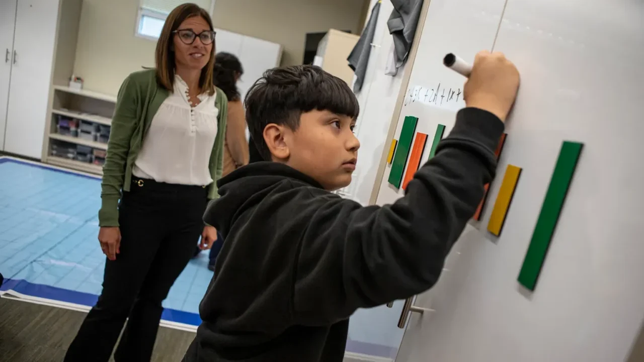 Image of a math coach helping a young male student who is writing on a whiteboard