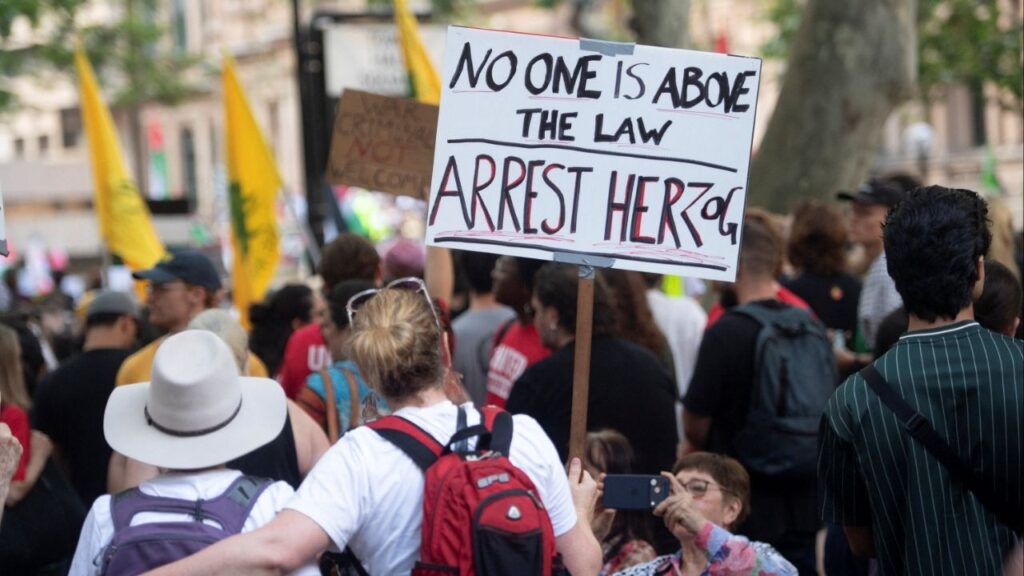 A protester holds a sign as demonstrators gather at Town Hall Square to protest against Israeli President Isaac Herzog's state visit to Australia following a deadly mass shooting during a Jewish Hanukkah celebration at Bondi Beach on December 14, in Sydney, Australia, February 9, 2026. (Reuters/Jeremy Piper )