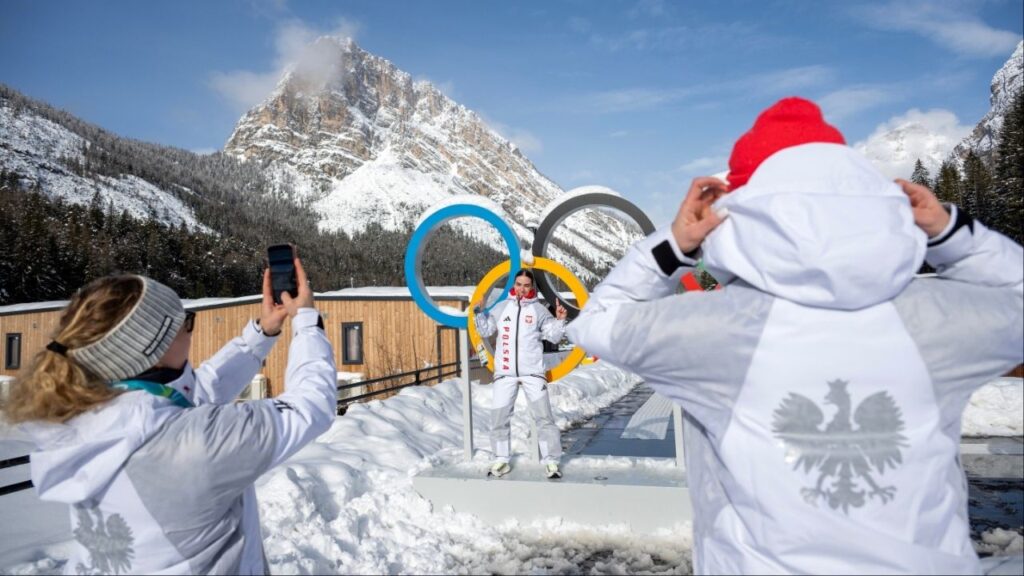 A sports fan poses for photos in front of the Olympic rings in Cortina d'Apezzo, Italy, on Thursday, Feb. 5, 2026. The Milan-Cortina Games are overlapping with a moment of geopolitical turbulence as conflicts rage, national leaders issue threats and alliances are strained. (James Hill/The New York Times)