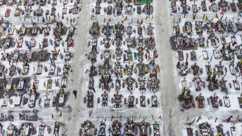 A visitor walks amid hundreds of graves of fallen Ukrainian soldiers in Lviv, Ukraine, Feb. 24, 2026. Some estimates indicate that Ukraine has lost more soldiers as a proportion of its wartime population than Russia has, even if Russian losses have been far larger overall. (Mauricio Lima/The New York Times)