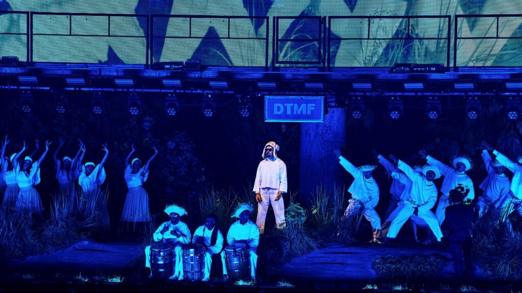 Image of Bad Bunny performing in Puerto Rico. He's in white and the stage is colored by blue lights.