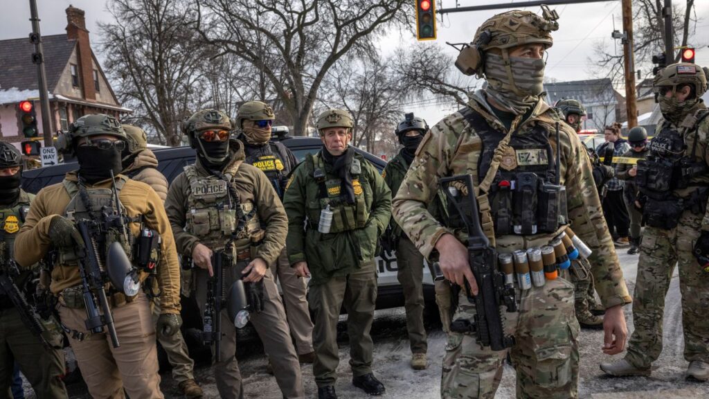 Image of Border Patrol Chief Greg Bovino unmasked and in full paramilitary gear alongside similarly dressed masked federal agents