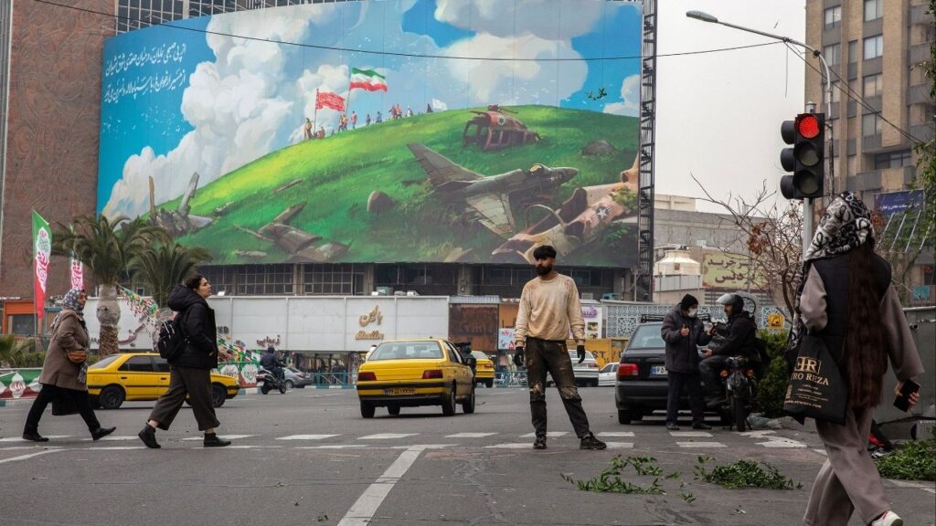 People cross the Valiasr Square, where there’s a new billboard showing American fighter jets being destroyed, in Tehran, Iran, on Feb. 7, 2026. Security officials are monitoring increasingly worrisome signs as President Trump considers another military campaign against Iran. (Arash Khamooshi/The New York Times)