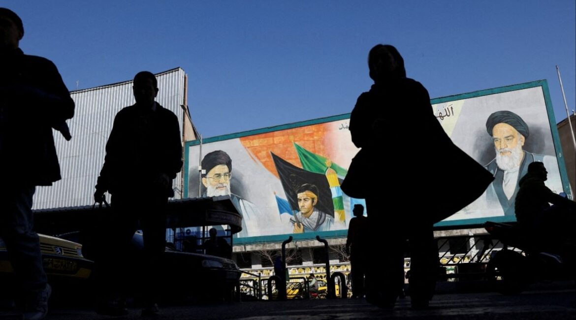 People walk near a mural featuring images of Iran's Supreme Leader Ayatollah Ali Khamenei and leader of Iran's 1979 Islamic Revolution Ayatollah Ruhollah Khomeini, on a street in Tehran, Iran, February 17, 2026. (Majid Asgaripour/WANA (West Asia News Agency) via Reuters)