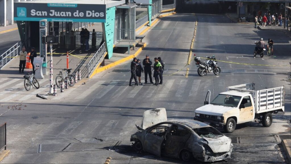 Police officers and civilians walk near the burned wreckage of a vehicle used as a barricade by members of organized crime following a series of detentions by federal forces, in Guadalajara, Mexico, February 22, 2026. REUTERS/Michelle Freyria