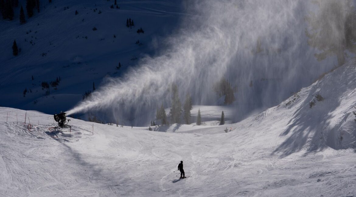 Image of a snowmaker blowing snow onto a ski slope that has a solitary skier.