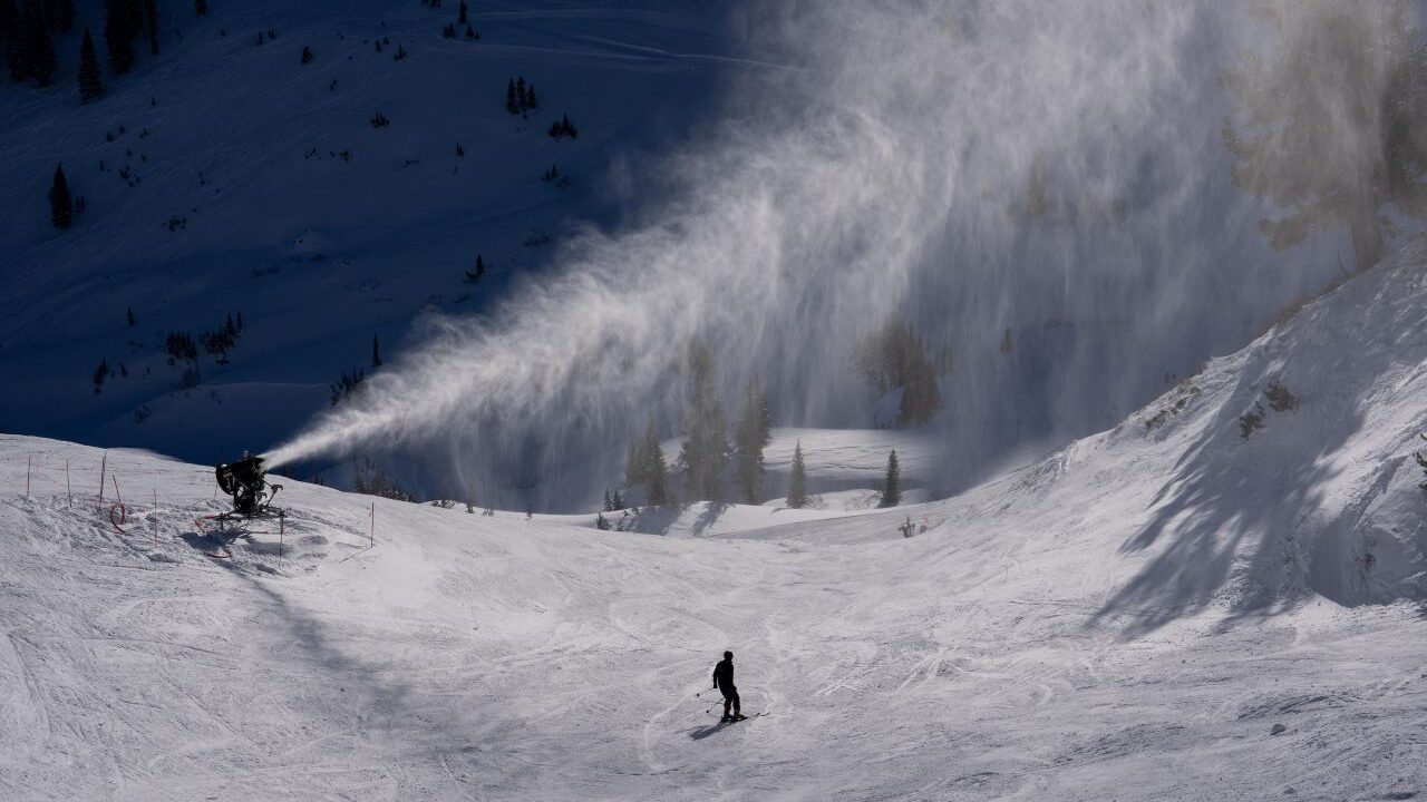 Image of a snowmaker blowing snow onto a ski slope that has a solitary skier.