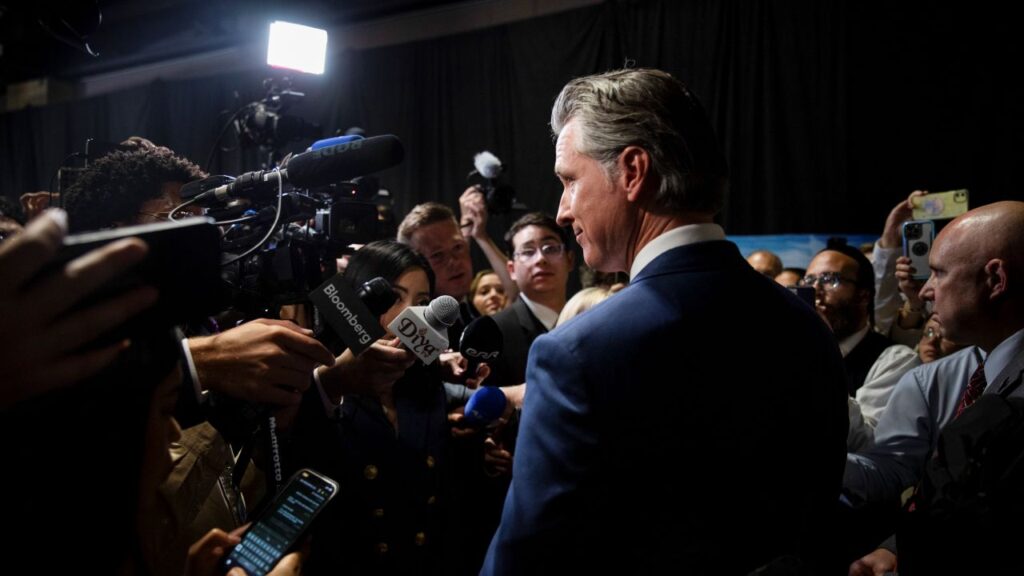 Image of California Gov. Gavin Newsom in a dark suit surrounded by the media