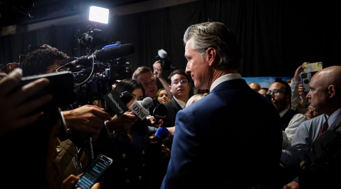 Image of California Gov. Gavin Newsom in a dark suit surrounded by the media