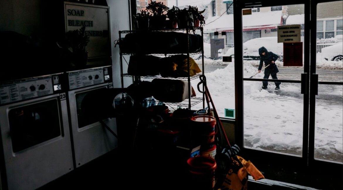 Shoveling snow outside of a laundromat in Queens, on Monday, Feb. 23, 2026. The powerful winter storm pummeling a vast swath of the Eastern Seaboard intensified on Monday morning, dumping snow at a furious rate and strangling major metropolitan areas at the dawn of the workweek. (José A. Alvarado/The New York Times)