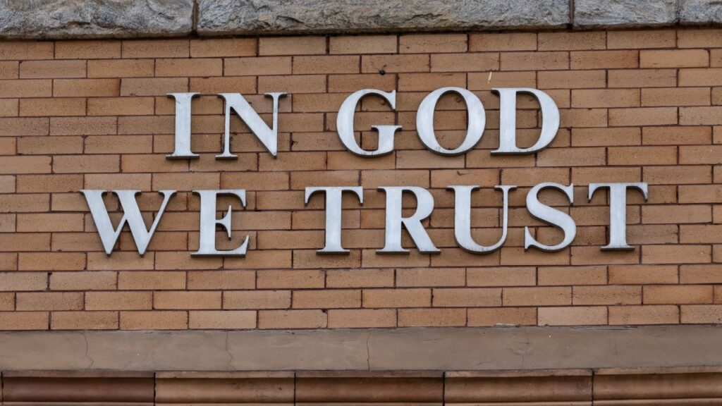 Image of the words "In God We Trust" on the exterior of a brown brick buildings
