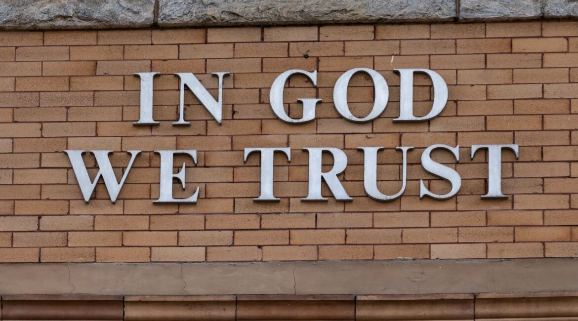 Image of the words "In God We Trust" on the exterior of a brown brick buildings