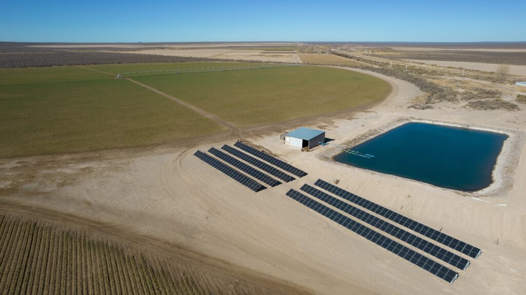 Image of a farm, solar panels, and a basin to store pumped water