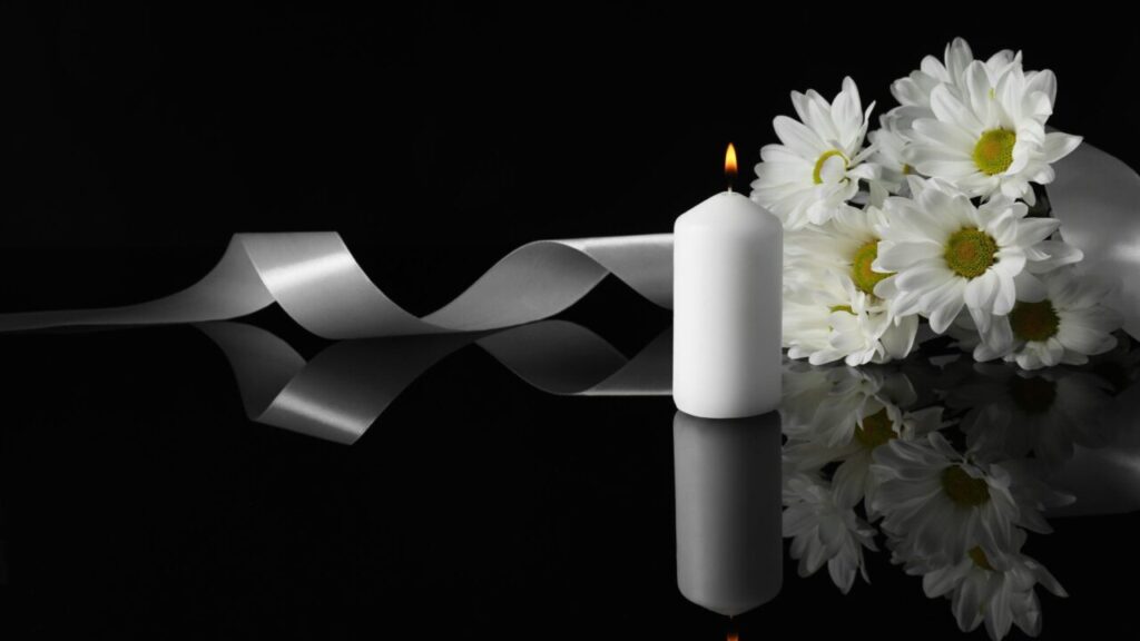 Image of a white burning candle and flowers against a black background symbolizing a memorial service
