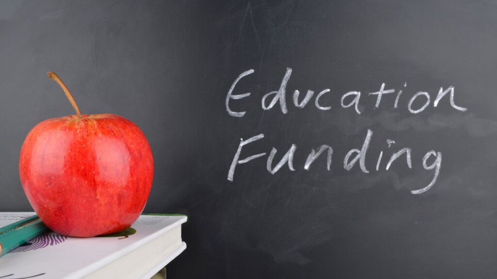 Composite image of a red apple, book, and the words "education funding" on a black chalkboard