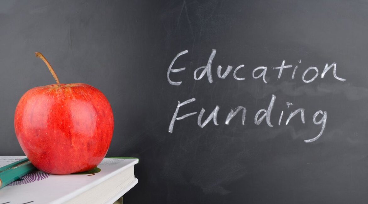 Composite image of a red apple, book, and the words "education funding" on a black chalkboard