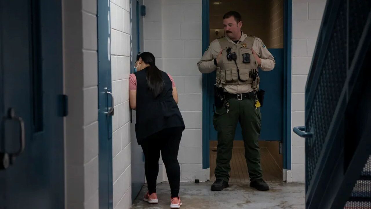 Image of a mental health worker speaking through a jail door to an inmate while a correctional officer watches